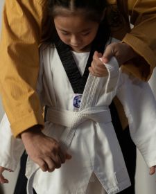 Senior tieing a white taekwondo belt on a girl